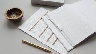 Schreibuntensilien wie Heft, Bleistift und Büroklammern in einer Schale