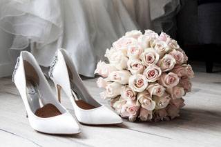 Weiße Brautschuhe und weißer Brautstrauß vor Brautkleid