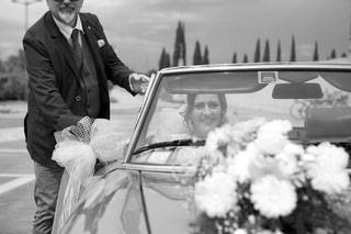 Schwarzweißfoto einer Braut in Brautauto mit Hochzeitsplaner daneben