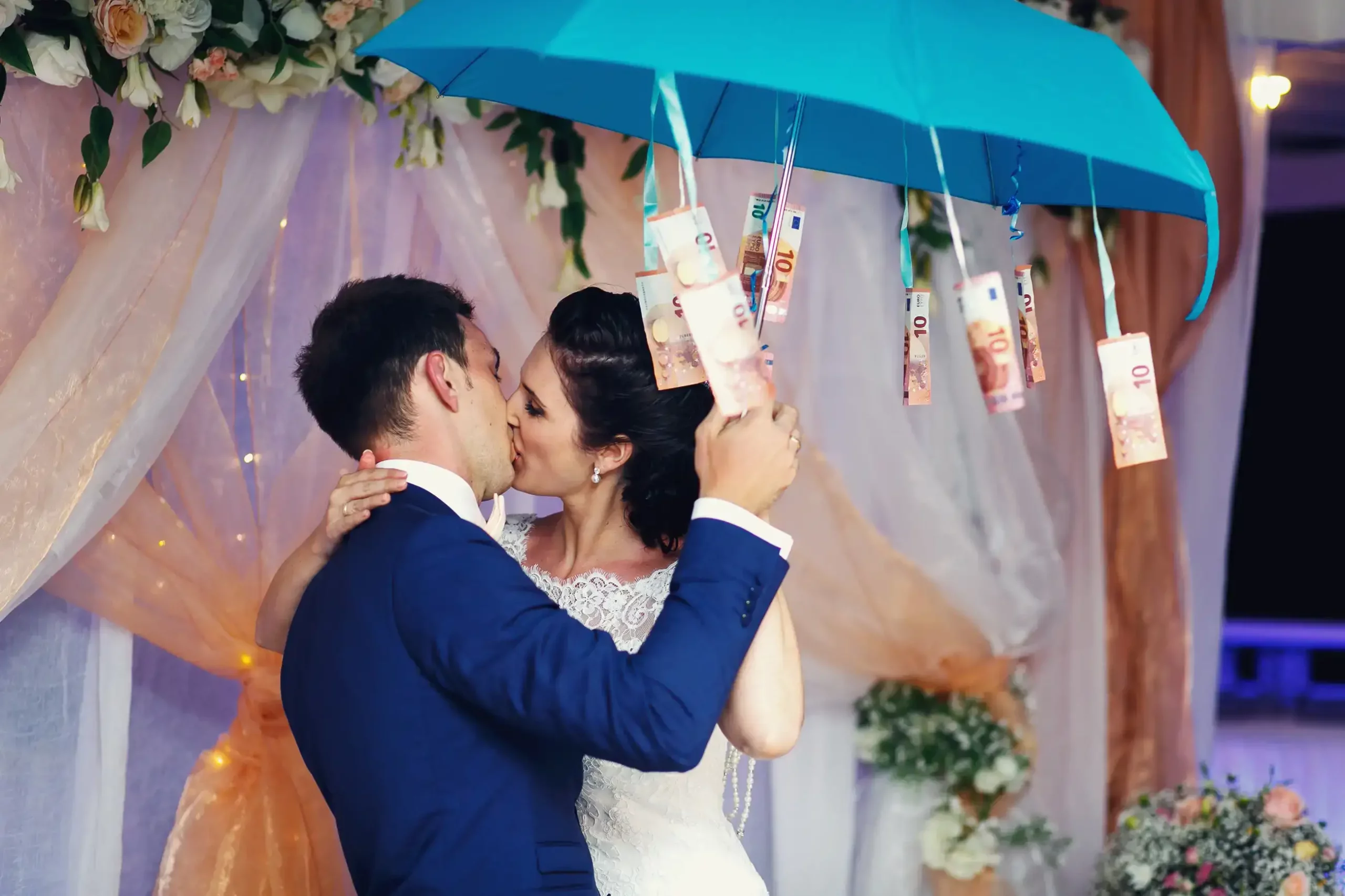 Brautpaar küsst sich unter Regenschirm voller Geldscheinen als Symbol für die Hochzeitsplaner kosten