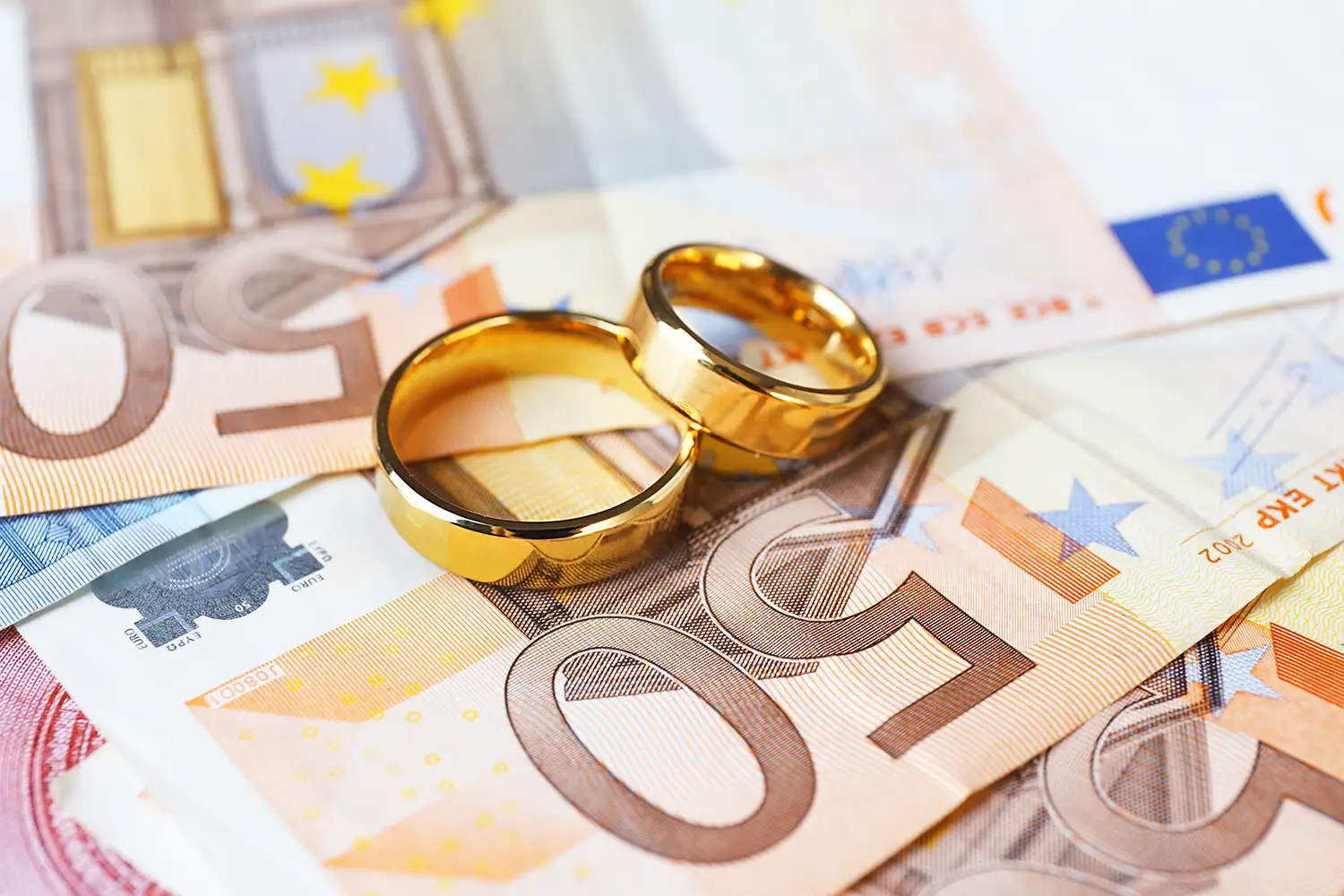Symbole für eine freie Hochzeit: Goldene Eheringe auf Euro-Banknoten Hintergrund